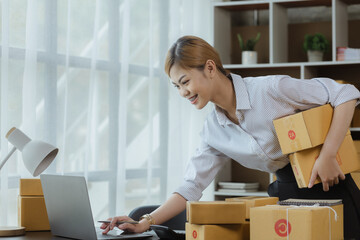 A beautiful Asian business owner opens an online store, she is checking orders from customers, sending goods through a courier company, concept of a woman opening an online business.