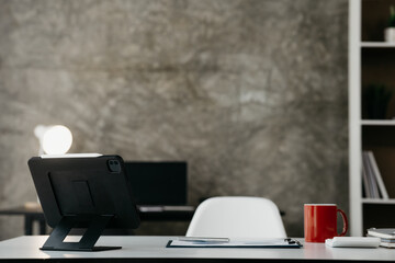 Modern loft style company office office room, desk in room with tablet and red coffee mug, empty office room in startup company office. The idea of arranging the office room.