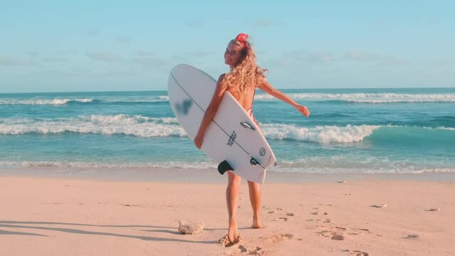 Slow motion shot of woman run to ocean wave with surfboard, back view camera follow. Female surfer on sunny day at beach laughing and smiling, happy to be sport outdoor to stay healthy and fit.