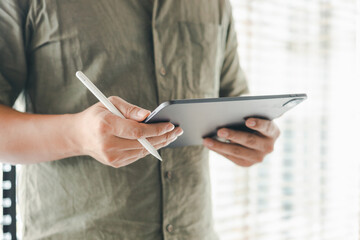 Business man in shirt using tablet standing near window at modern co-working office, surfing web. Focused guy browsing internet.