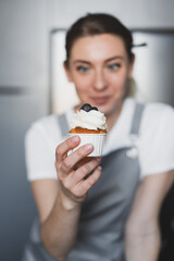 Young lovely woman pastry chef decorates cupcakes with whipped cream and having fun at home
