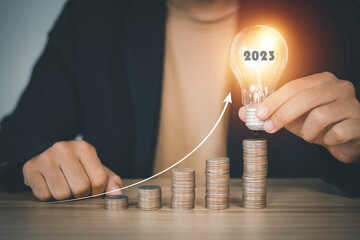 businessman holding a bright light bulb and an arrow pointing up The idea begins with a new invention. Get creative with new investments or jobs in 2023.