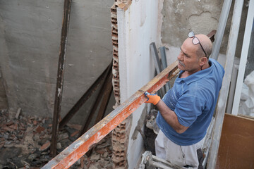 Mature mason removing old metal beams in a construction house.