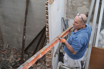 Fototapeta na wymiar Mature mason removing old metal beams in a construction house.