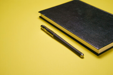 Black hardcover notepad and ballpoint pen on yellow background, close up, business and education...