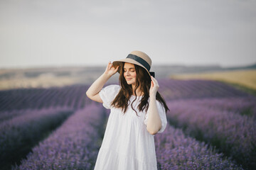 Young beautiful woman in white dress enjoying fragrance of lavender field.