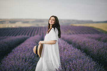 Fototapeta na wymiar Young beautiful woman in white dress enjoying fragrance of lavender field.