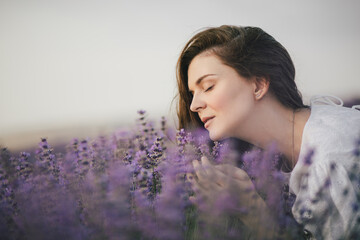 Young beautiful woman in white dress enjoying fragrance of lavender field.