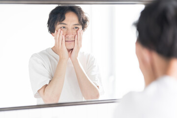 鏡の前で肌のケアをする若い男性/メンズビューティ