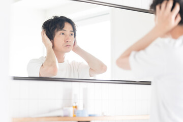 鏡でを見ながらヘアスタイリングする若い男性、メンズビューティー 