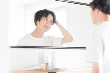 鏡を見ながらヘアセットする若い男性、メンズビューティ