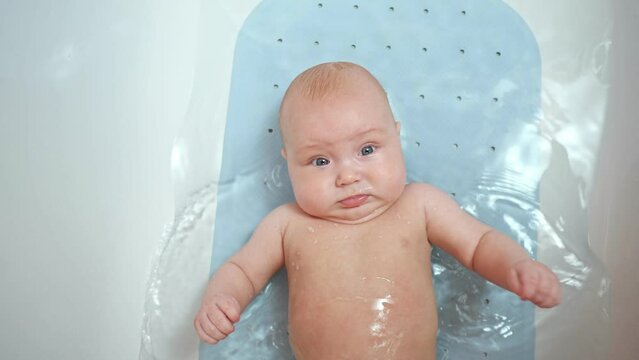 Hygienic procedures for newborn. Bathing the baby in the bathroom, slow motion. Happy baby in bath, top view.