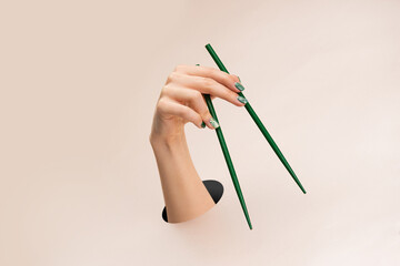Female hand holding green chopsticks downward on clean pink background