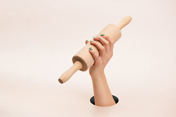 Female hand holding wooden rolling pin on clean pink background