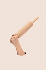 Strong female hand holding wooden rolling pin on clean pink background