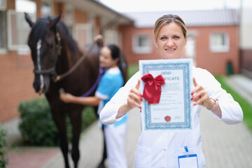 Woman veterinarian holds medical certificate on background of horse