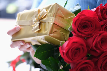 Bouquet of red roses and golden gift box in female hands