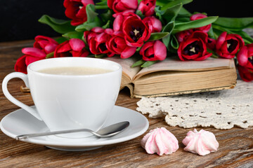 Cup of coffee, book, marshmallow, tulips and knitted napkin on wooden table 