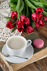 Cup of coffee, book, macaroon, tulips and knitted napkin on wooden table 