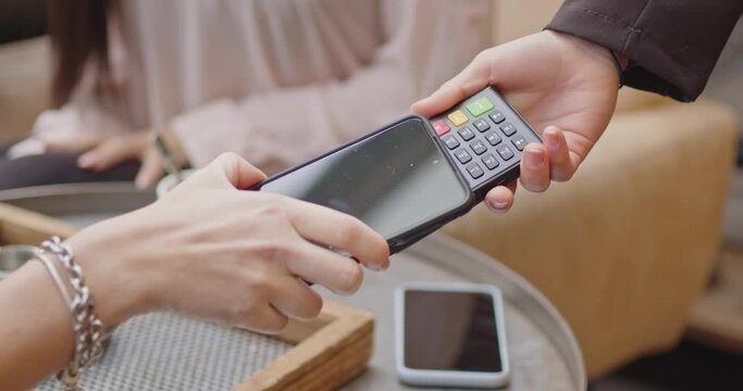 Pay by phone on electronic payment machine or card reader. E-money at cashless wallet. Female client hand on pos-terminal of female seller or store employee at coffee place or restaurant closeup