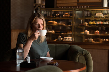 Beautiful blonde woman sits alone in coffeehouse and drinks coffee and using phone