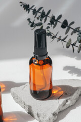 Amber pump bottles with serum, tonic or essential oil on grey concrete podium with eucalyptus branches. White background with daylight. Beauty concept for face and body care