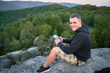 Man operating drone using remote controller. Man using drone at sunset for photos and video making while sitting on top of high boulder in the mountains.
