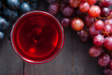 glass of red wine and grapes on black wooden table background