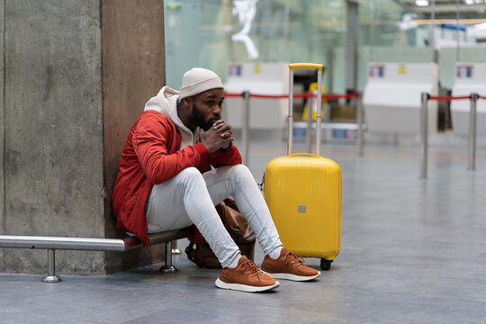 Sad African American man upset at airport his flight is delayed. Depressed traveler male waiting for a plane sitting in empty terminal with baggage. Exhausted guy on a long night connection at airport