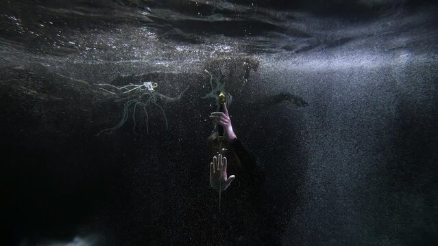 the long-haired man bowed before the sword. a woman with pearl beads hovers behind him in the dark water with bubbles