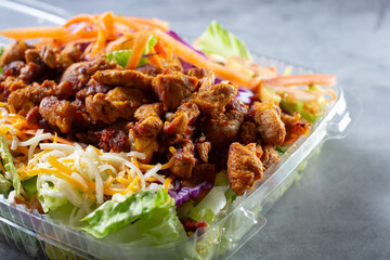 A closeup view of a pollo asado salad inside a plastic to go container.