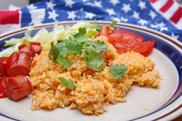 Fried rice with tomato sauce served in a white plate with fillings and sautéed tomatoes on an American flag-themed table.