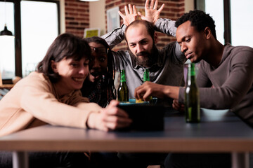 Cheerful diverse people with modern smartphone device taking selfie group photo together. Positive young adult people sitting at home in living room with mobile cellphone while taking picture.