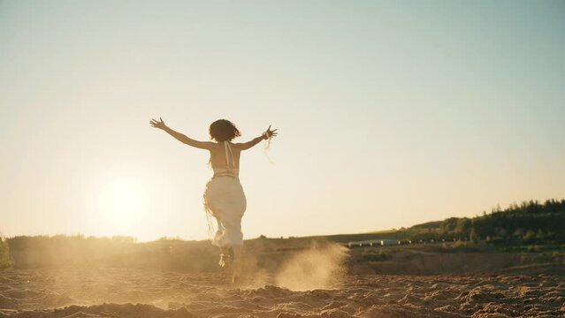 4k video of young woman in lilnen skirt running on sand. Sunset cinematic consept. Hand wide open. Ethnic and boho style.