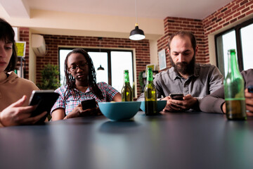 Cultural diverse people sitting in living room while browsing internet on modern smartphone devices. Multiethnic friends sitting at home while watching online video content on mobile phones.