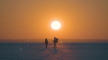 Fototapeta premium The two travelers walking through the snow field on sunset background