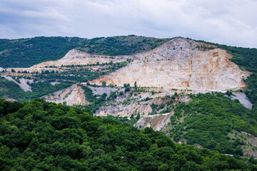 Fototapeta na wymiar Natural quarry is located near road against backdrop of Rhodope Mountains and hills with forests and mountain vegetation