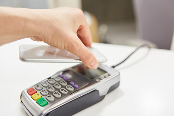 Hand holds smartphone via NFC reader when paying