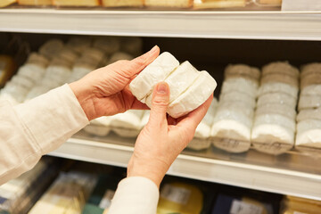 Customer at the refrigerated shelf holds soft cheese in his hands