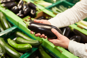Customer at the weekly market holds eggplant in his hands