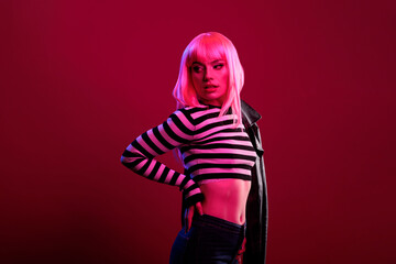 Portrait of attractive girl with leather jacket posing in dark pink light, using fluorescent lighting in studio to take pictures. Cool stylish rocker with funky hairstyle and punk clothes.