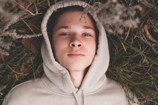 Sad And Depressed Teenager Boy 16-18 Year Old Wear Hoody Lying On Ground Outdoors. Autumn Season.