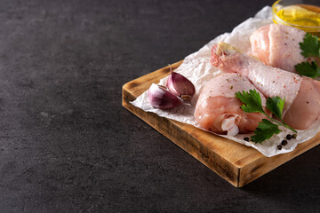 Raw chicken meat legs with spices and herbs on black background. Copy space