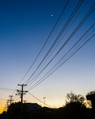 Waxing crescent moon over silhouette powerlines at dawn. Auckland. Vertical format.