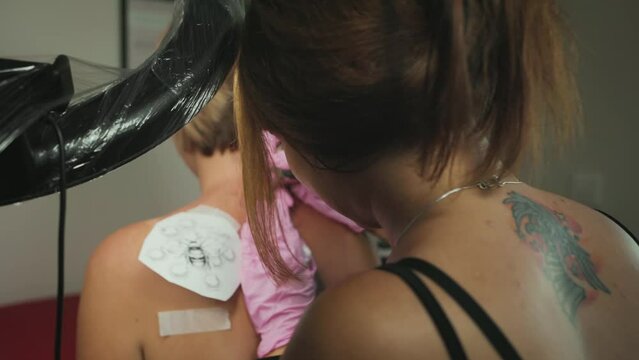 World tattoo day. A tattoer makes a tattoo to a client. Back view and zoom out. Close up. Real time.