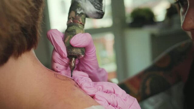 A tattoer makes a tattoo to a client's back. Close up of hands in latex gloves and tattoo machine. Real time.