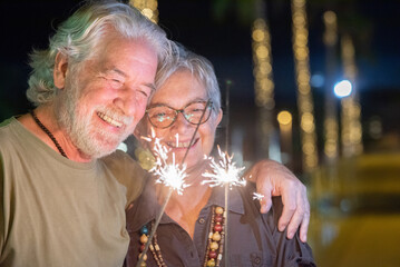 Close-up on beautiful senior couple in outdoor at night having fun with sparkles lights. Two...