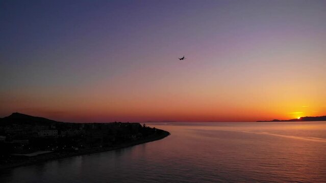 drone flight over ialysos beach and the mediterranean sea at sunset with a passing plane against the orange sky