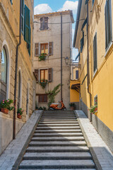 Fototapeta na wymiar View of Carrara (Tuscany): glimpse of a typical italian alley with a marble staircase and flowers hanging from the balconies