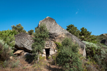Porta de entrada de uma casa em baixo de uma enorme pedra a meio do monte. Casa antiga em ruínas construida entre rochas enormes
 - obrazy, fototapety, plakaty